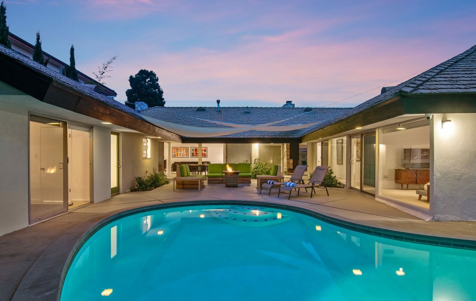 Courtyard pool at dusk surrounded by sliding glass doors at a furnished single-level home